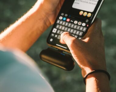 Close-up of a person texting on a smartphone connected to a power bank outdoors.