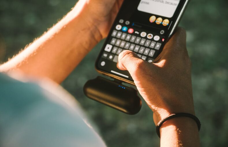 Close-up of a person texting on a smartphone connected to a power bank outdoors.