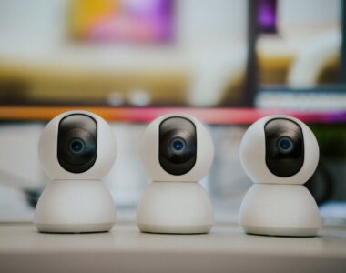 Three modern smart home security cameras placed on a table indoors with a blurry background.