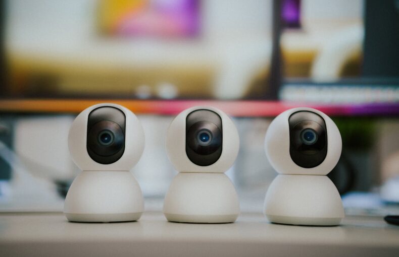 Three modern smart home security cameras placed on a table indoors with a blurry background.
